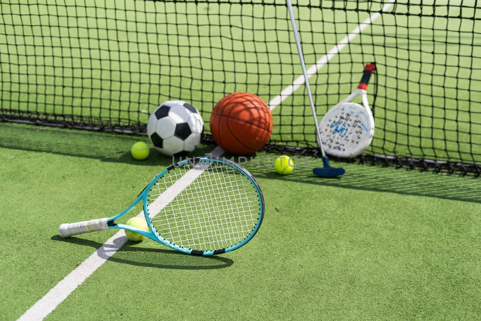 A variety of sports equipment including an american football, a soccer ball, a tennis racket, a tennis ball, and a basketball. High quality photo