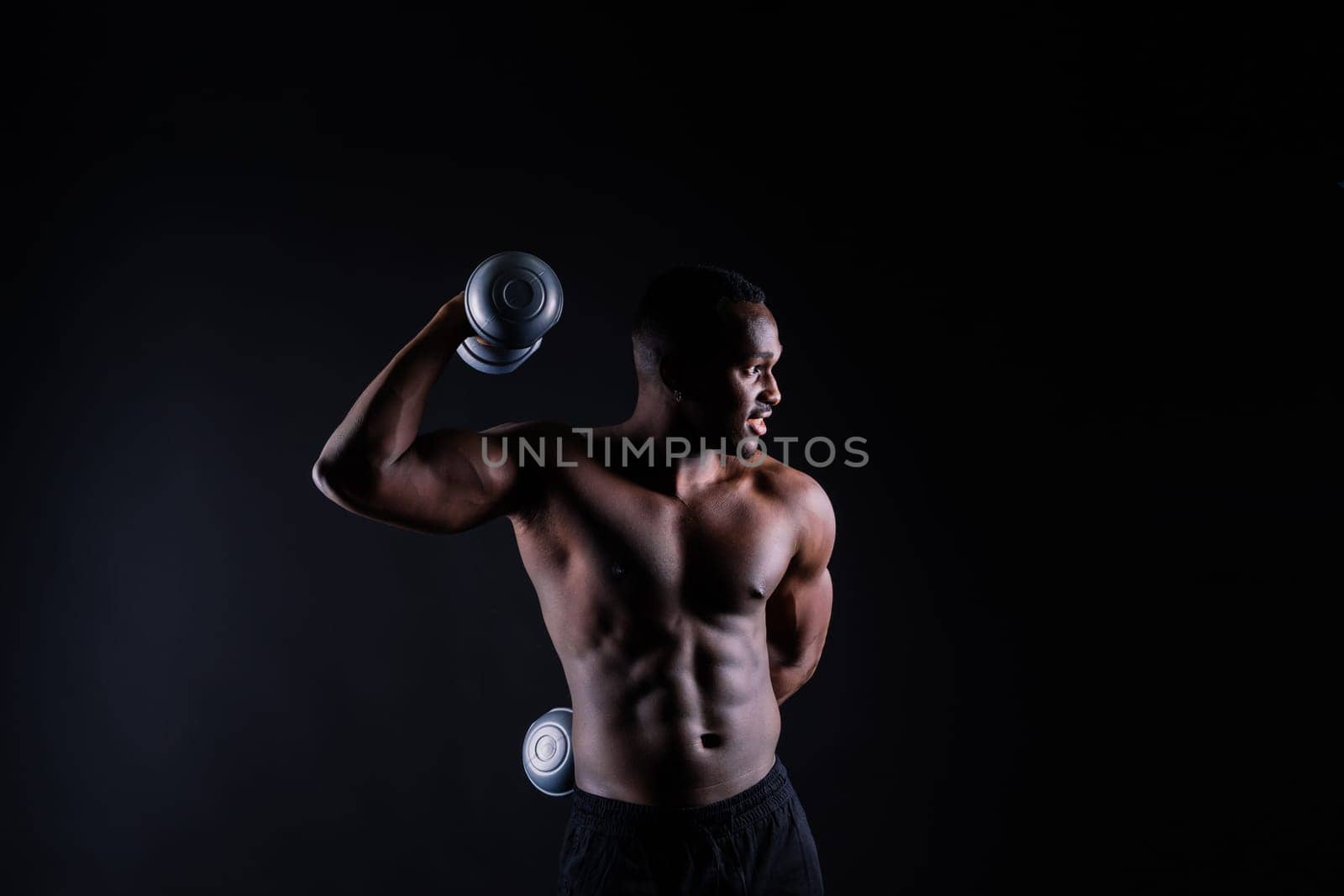 Isolated african muscular man with dumbbells on dark studio background. Strong shirtless black guy by Zelenin