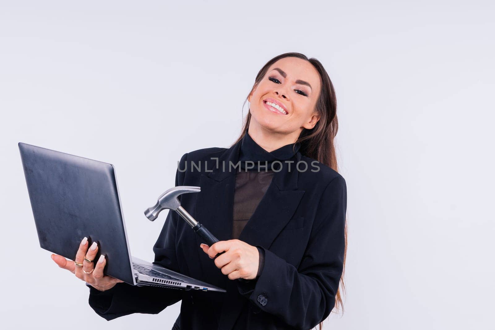 Attractive woman wearing business suit with computer angry facial expression holding hammer