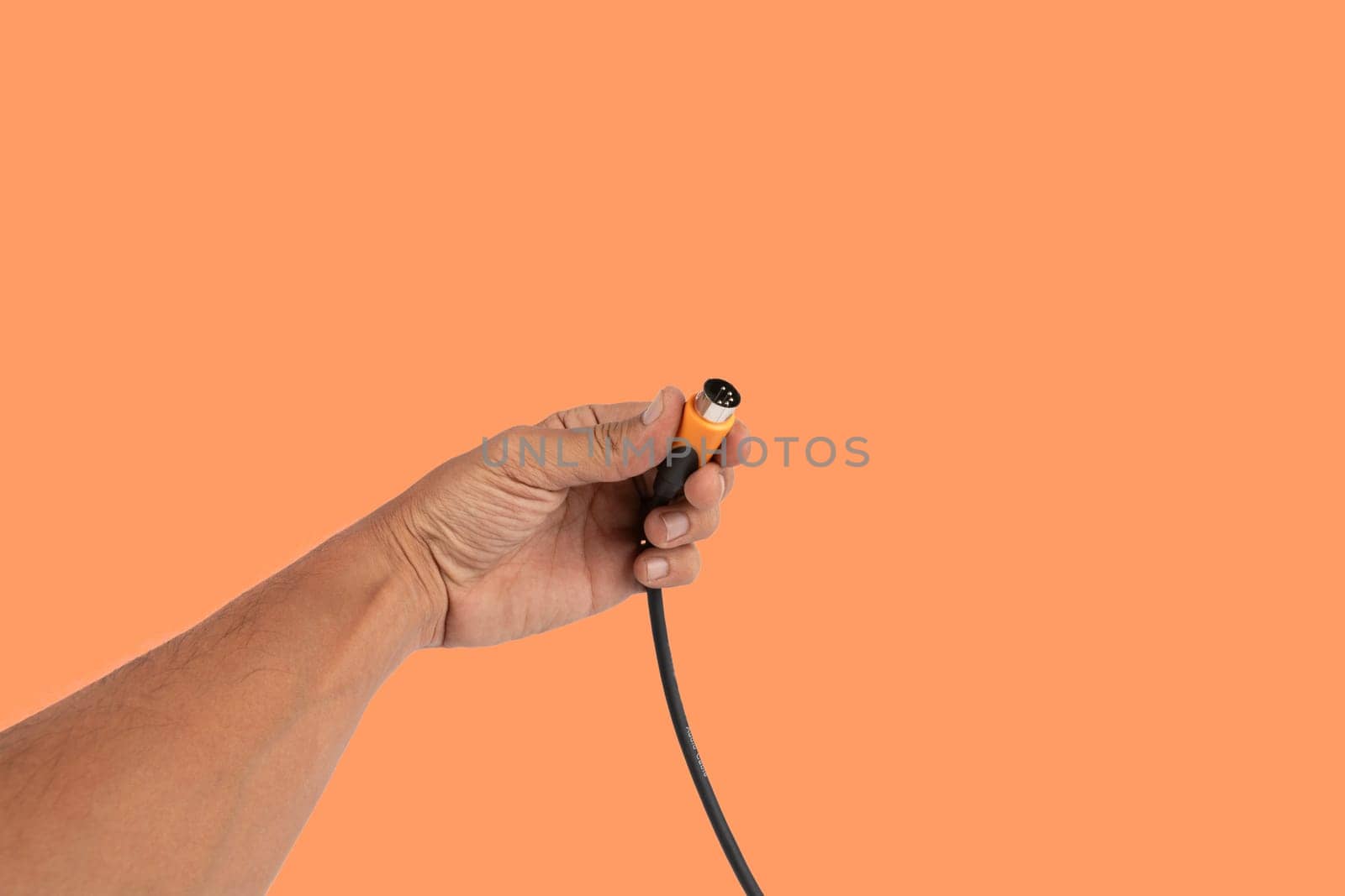 Black male hand holding a MIDI audio cable isolated on orange background by TropicalNinjaStudio