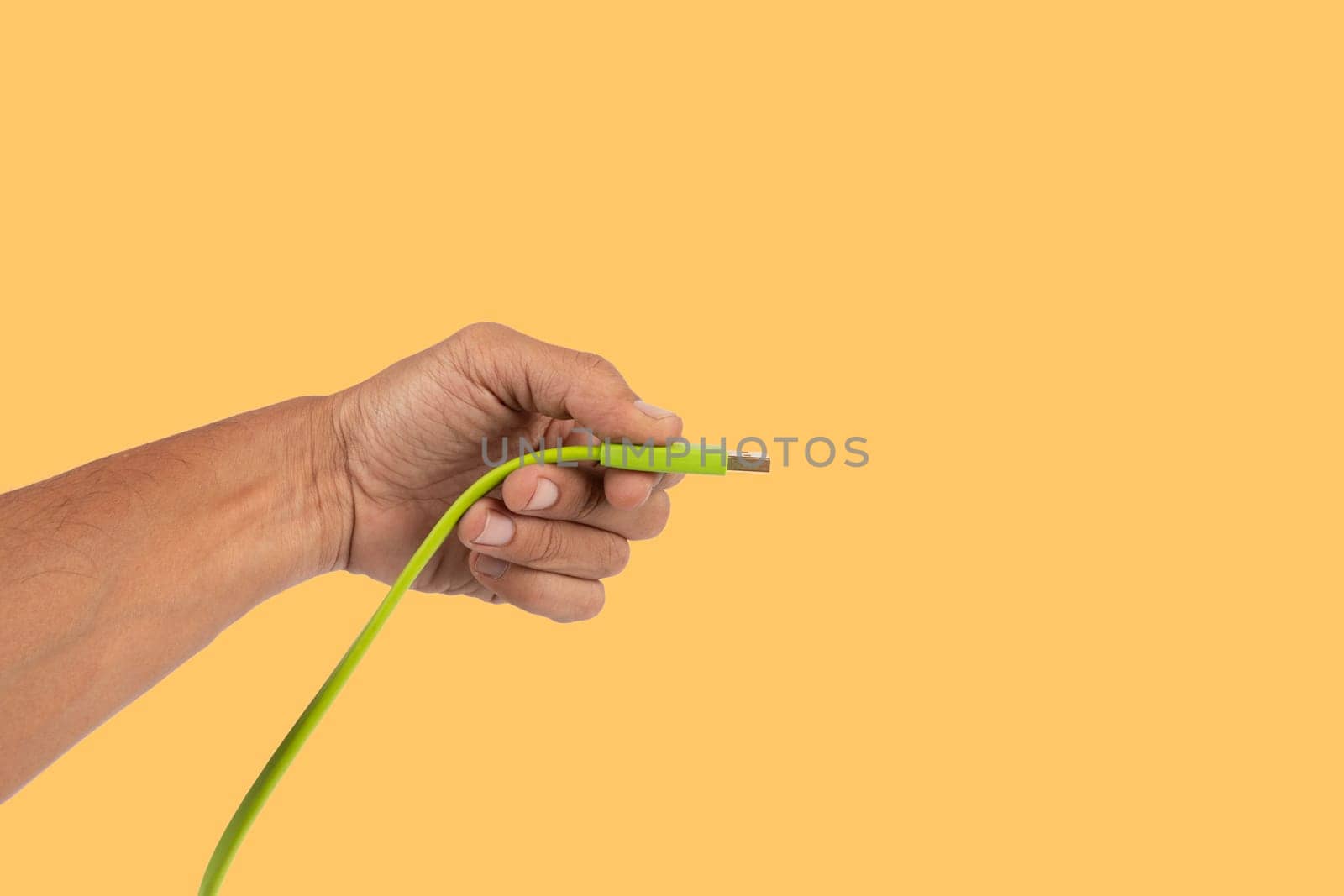 Black male hand holding a green USB cable isolated on yellow background. High quality photo