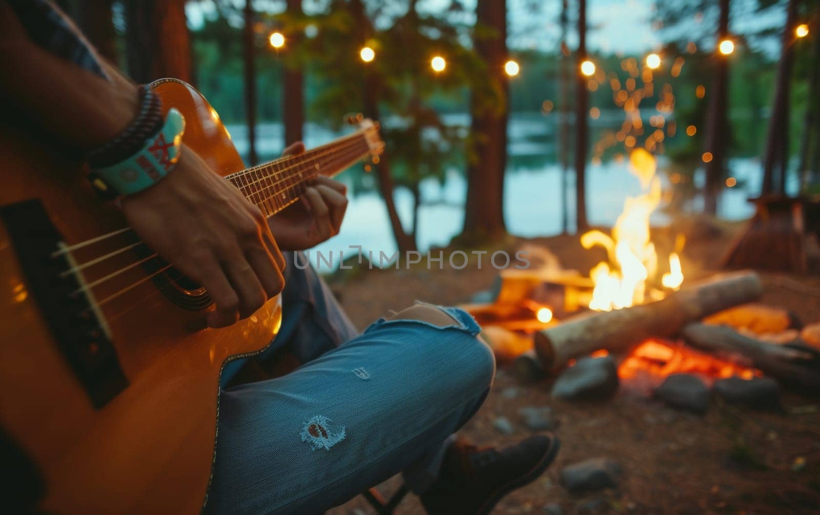 Person playing an acoustic guitar by a campfire near a tranquil lake at dusk