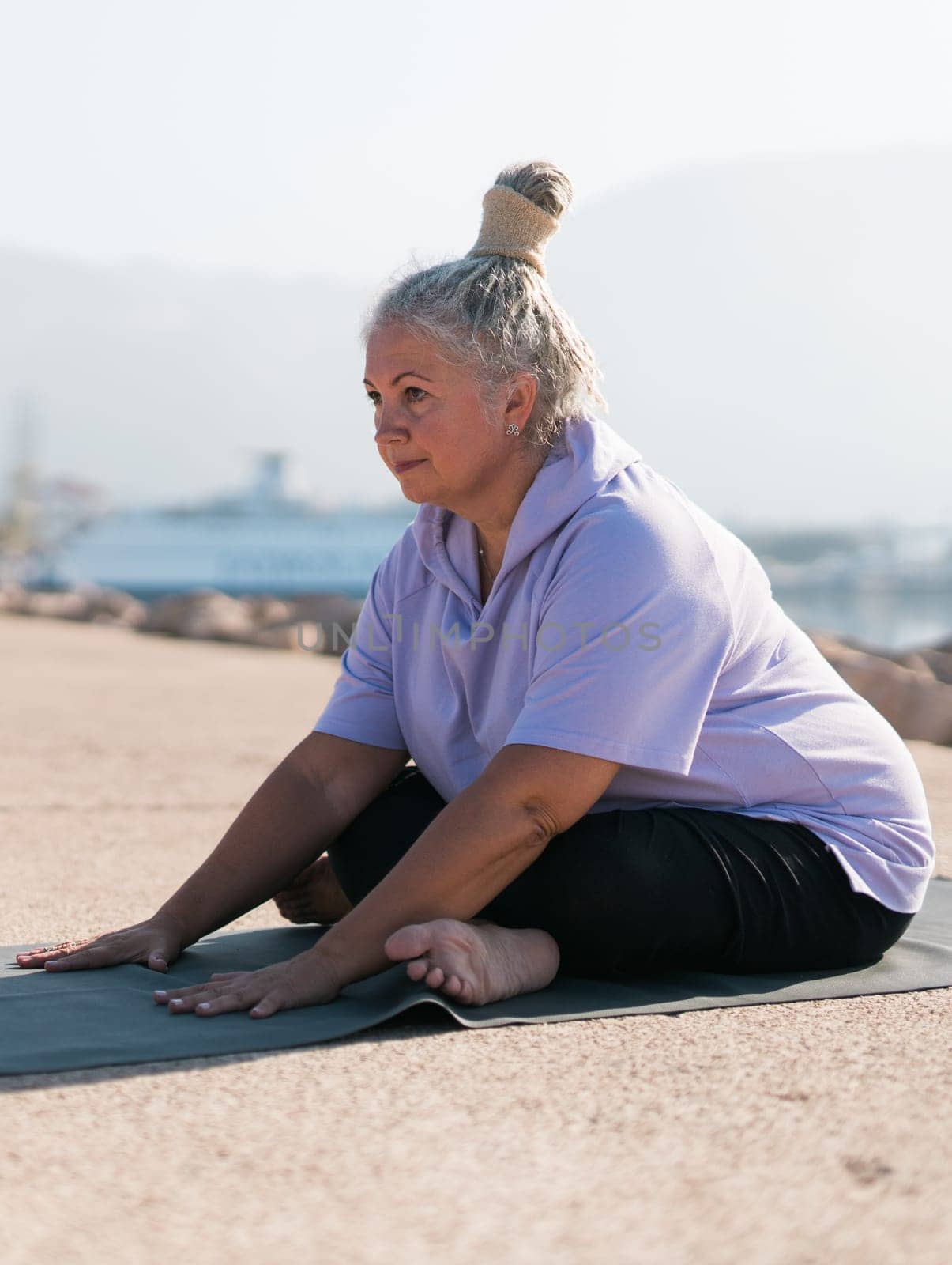 Mature woman with dreadlocks working out doing yoga exercises on sea beach - wellness well-being and active elderly age.