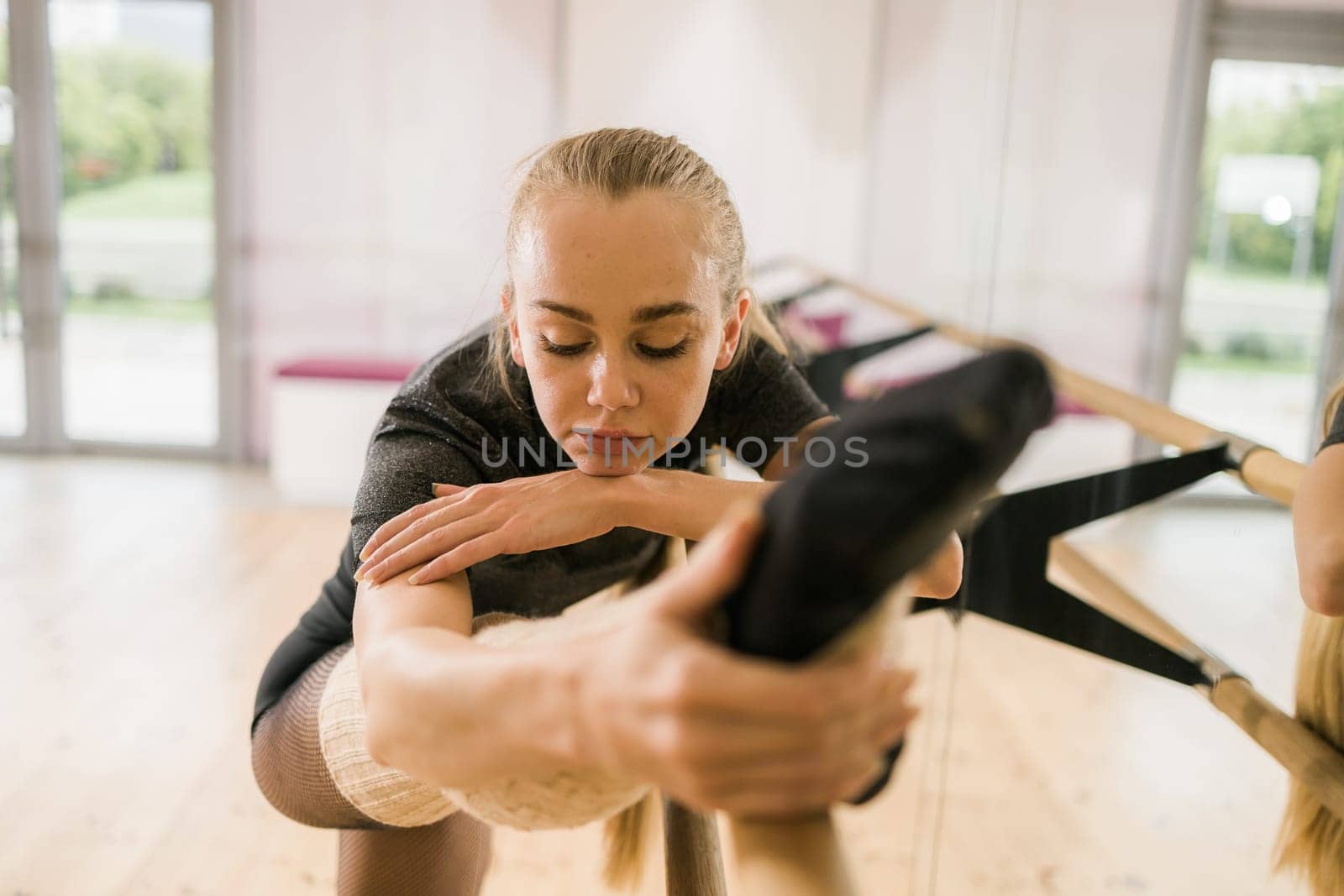 Young woman ballerina stretching and training at barre in dance studio - ballet and dancer