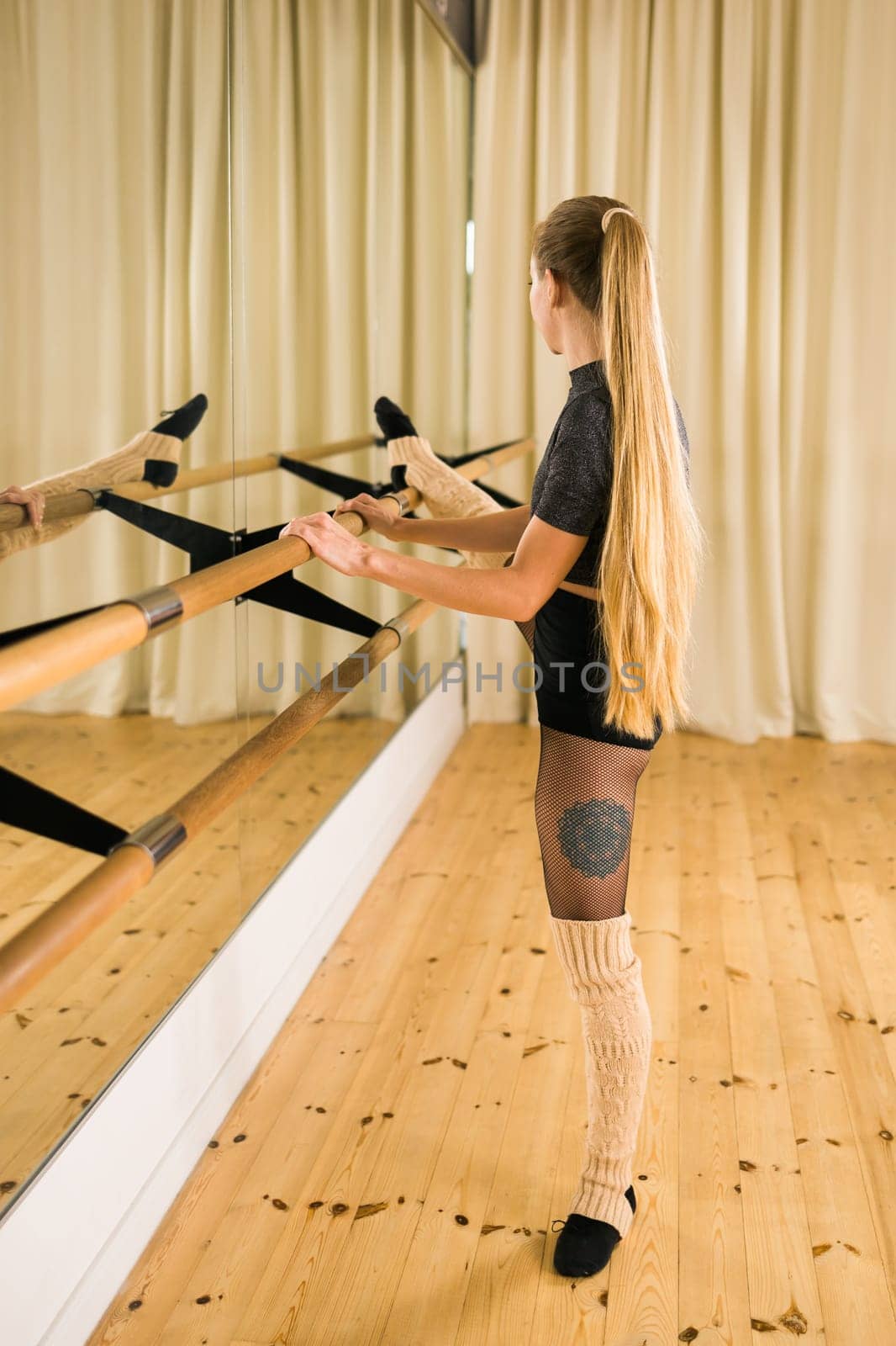 Young woman ballerina stretching and training at barre in dance studio - ballet and dancer concept by Satura86