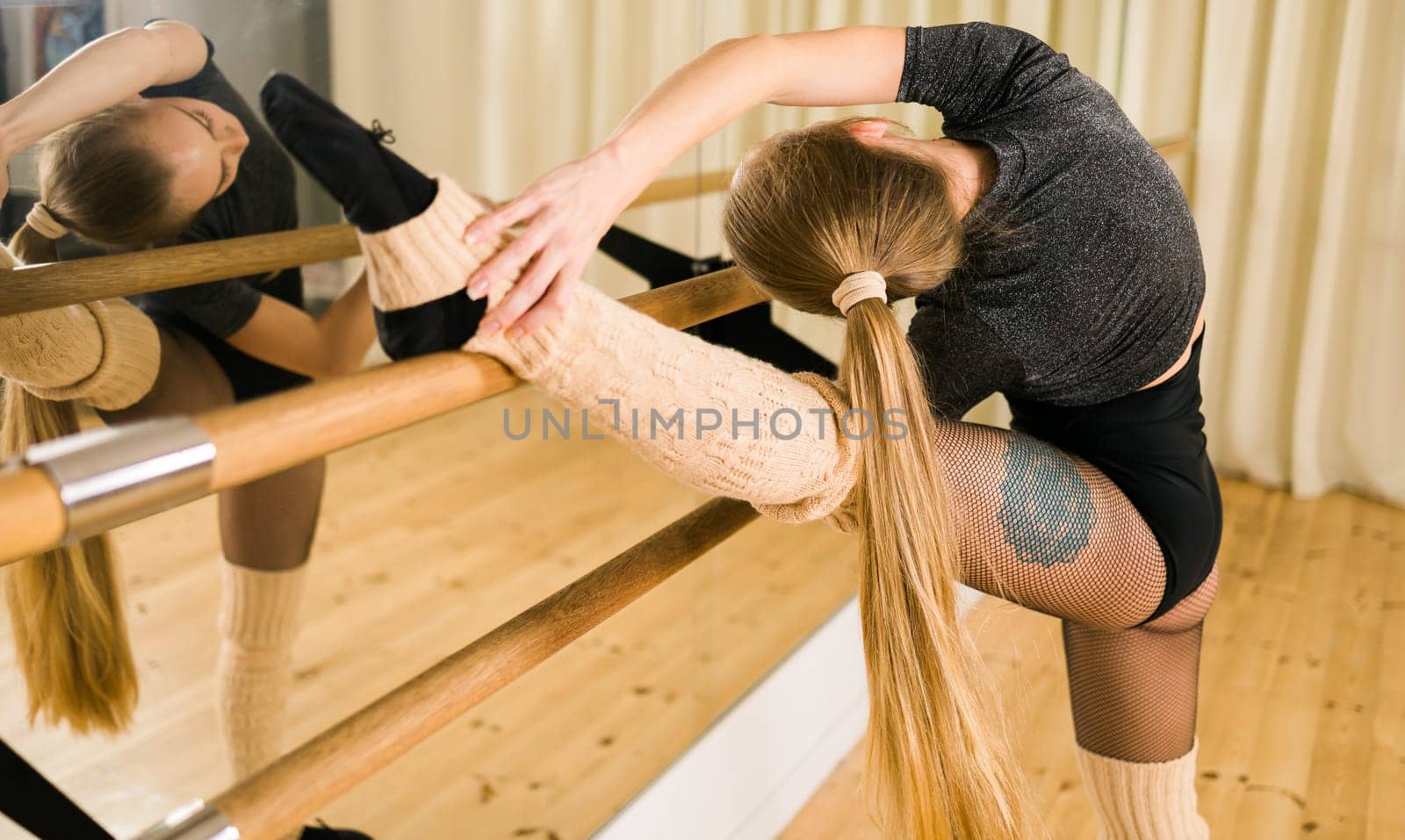Young woman ballerina stretching and training at barre in dance studio - ballet and dancer concept by Satura86