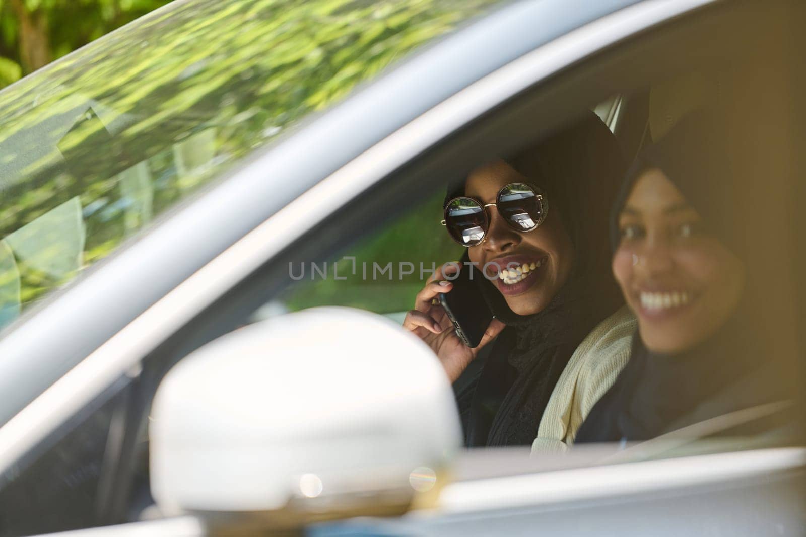 Two Muslim women wearing hijab converse on a smartphone while traveling together in a car through the.