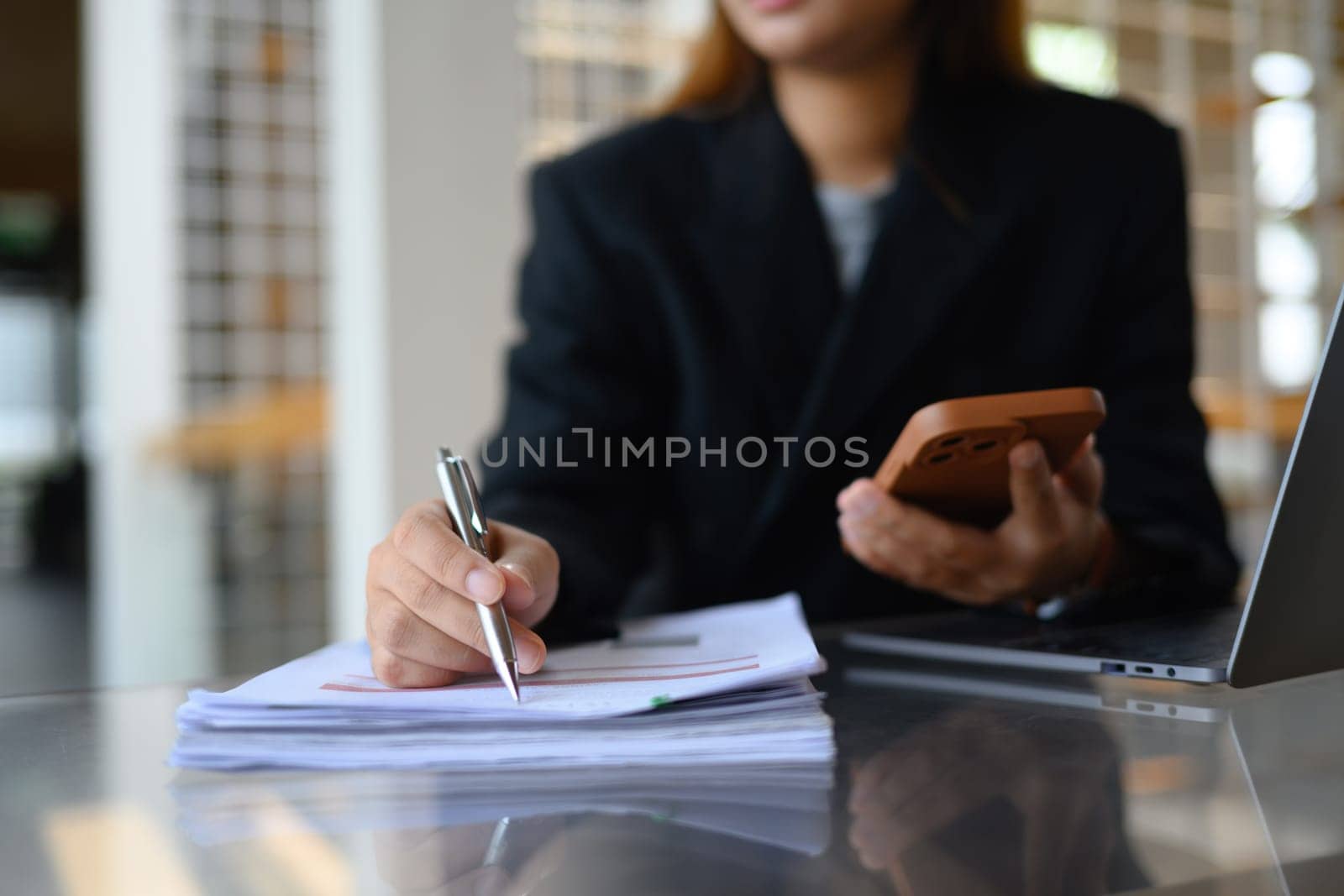 Professional businesswoman using mobile phone and checking financial reports at office.