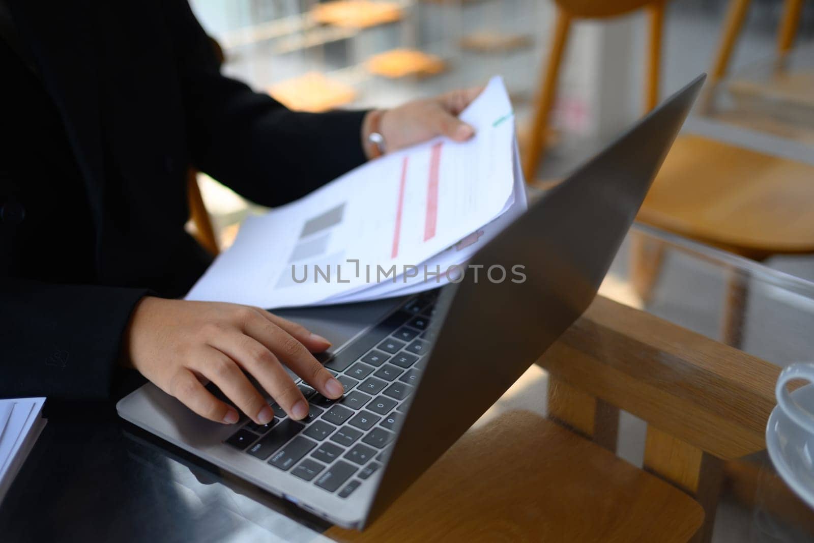 Finance Investment analyst holding documents and using laptop at office desk.