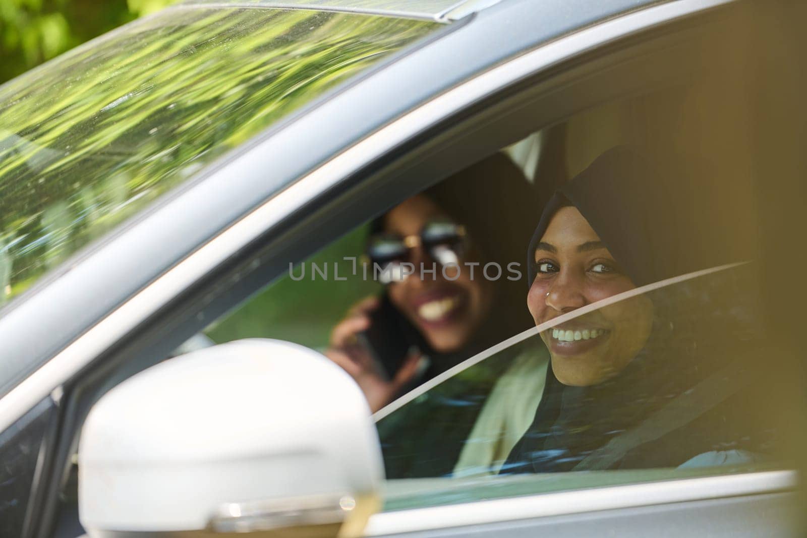 Two Muslim women wearing hijab converse on a smartphone while traveling together in a car through the.