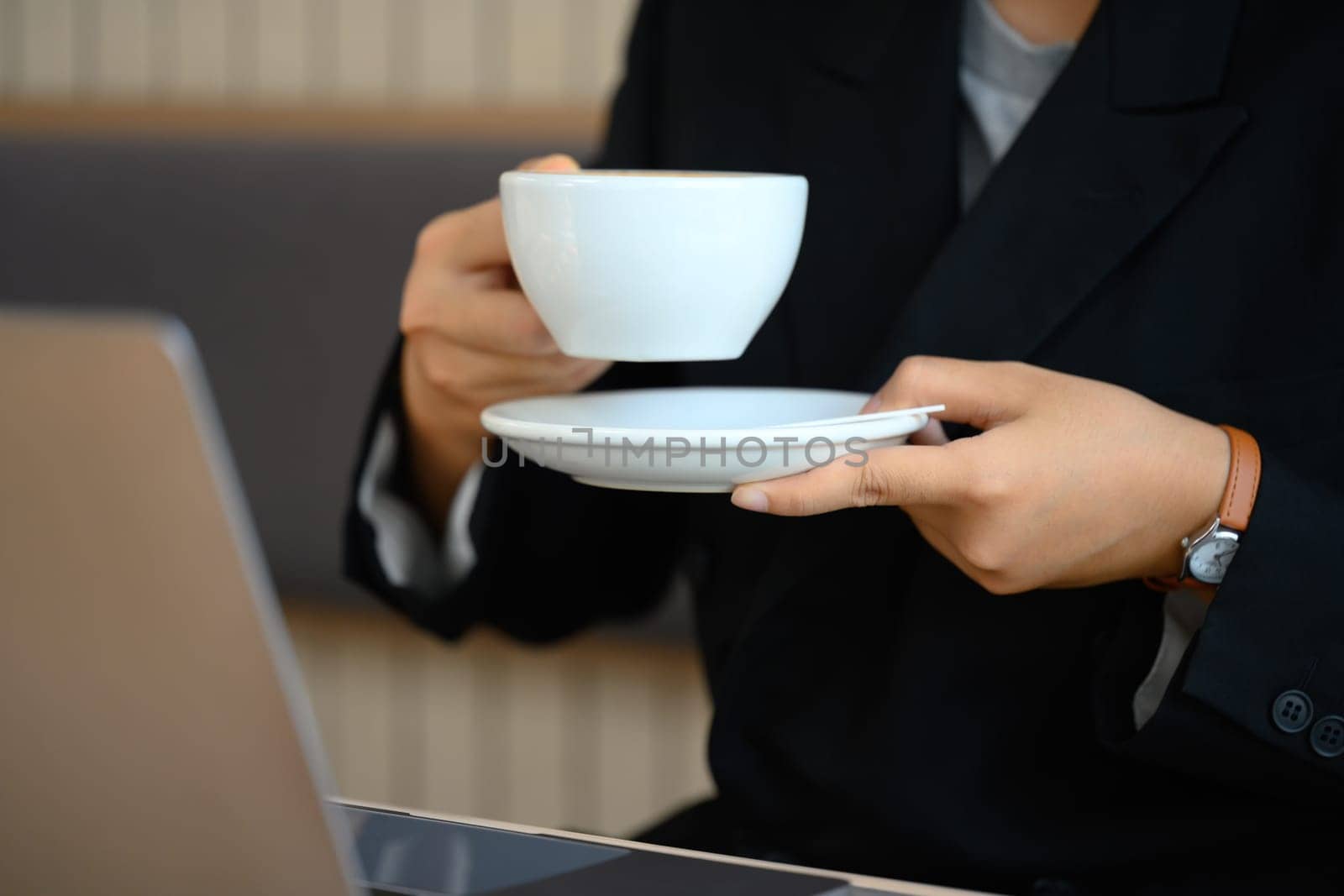 Businesswoman in black suit holding cup in hands taking break at her workplace.