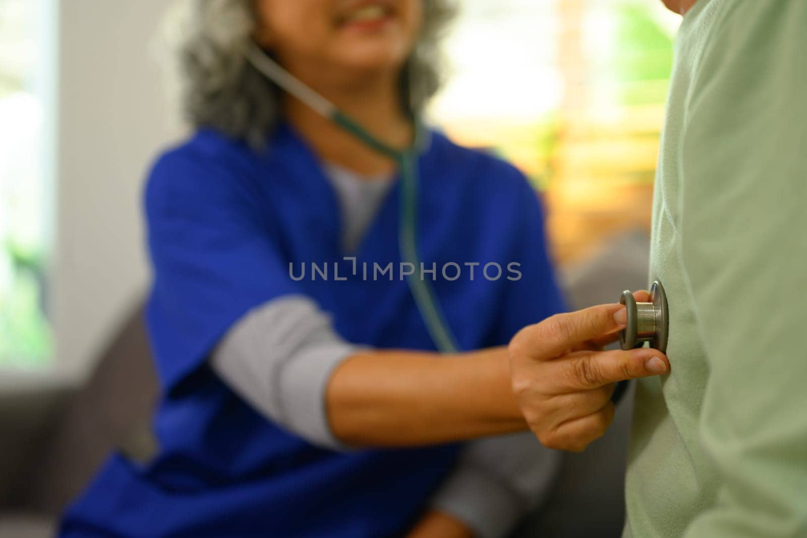 Female doctor listening to patient heartbeat during home visit. Health care concept.