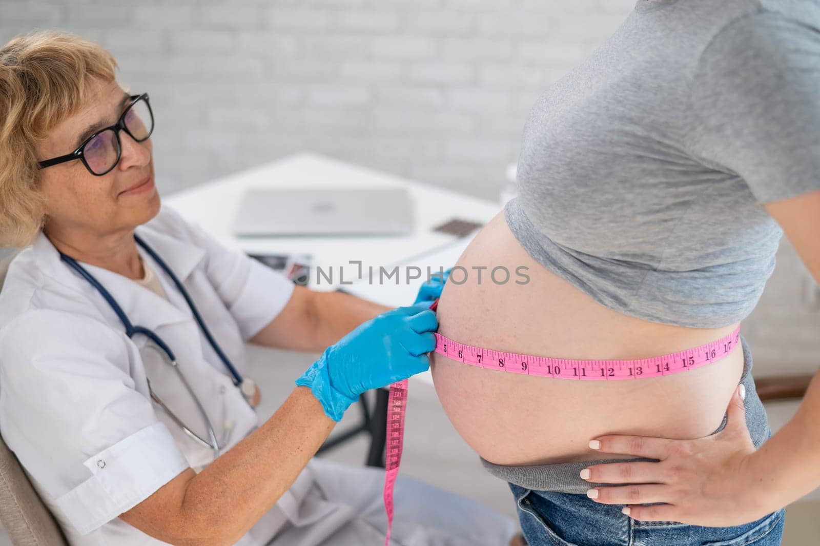 Doctor measuring the volume of a pregnant woman's abdomen using a tape in inches. by mrwed54