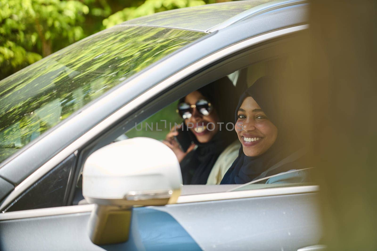 Two Muslim women wearing hijab converse on a smartphone while traveling together in a car through the.