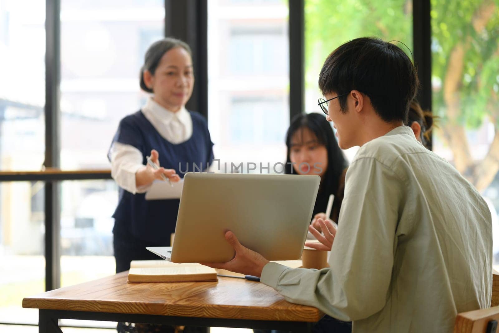 Young male student showing project on laptop to professor in classroom by prathanchorruangsak