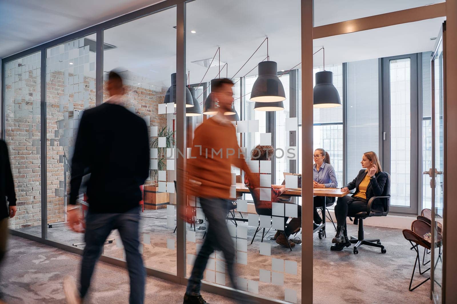 In the dynamic hustle and bustle of a business environment, a group of young business professionals walk down the corridor next to their office, while their colleagues collaborate inside, symbolizing teamwork and productivity by dotshock