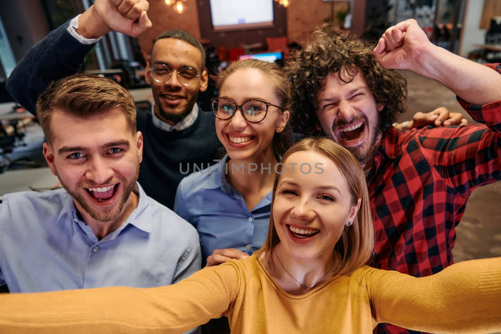 A diverse group of business professionals take a break from their tasks in a modern startup office to capture a creative selfie, showcasing teamwork and a vibrant workplace culture.