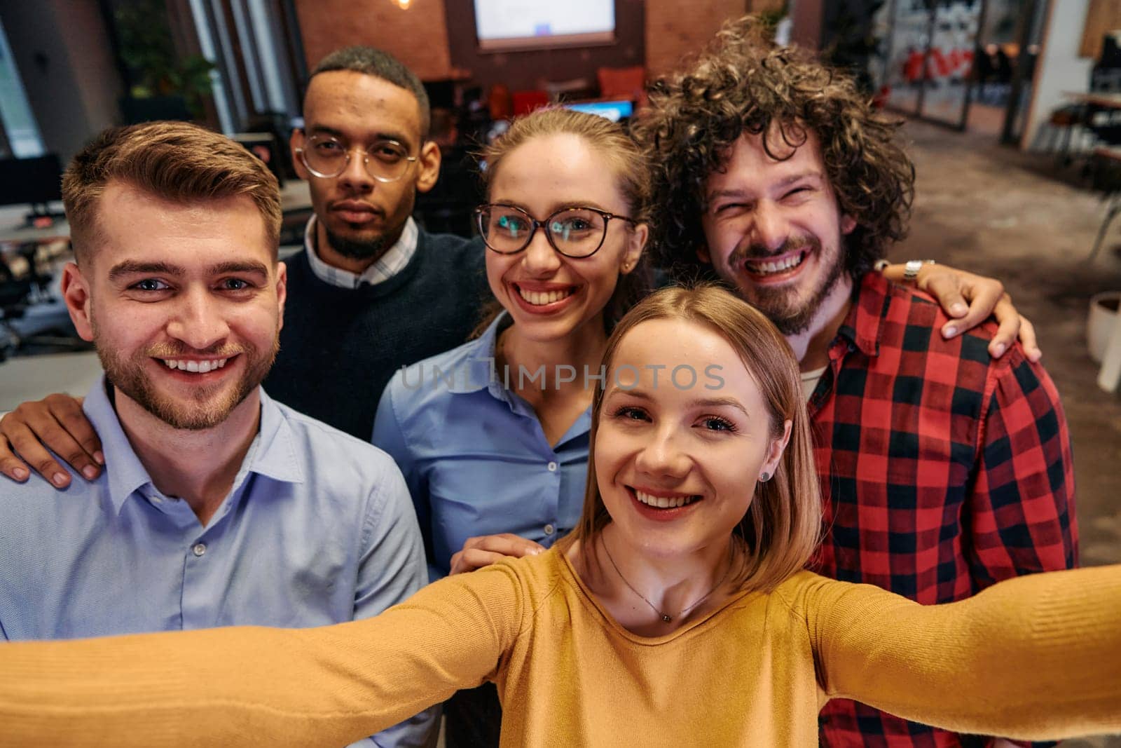 A diverse group of business professionals take a break from their tasks in a modern startup office to capture a creative selfie, showcasing teamwork and a vibrant workplace culture by dotshock