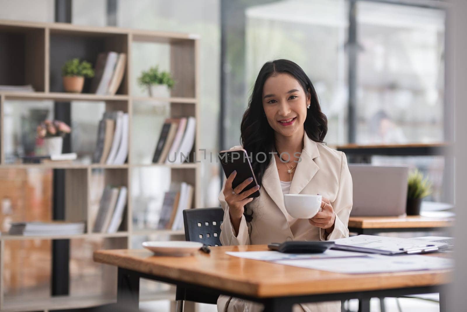 Beautiful businesswoman follows news on social media and drinks coffee at her desk in the morning. by wichayada