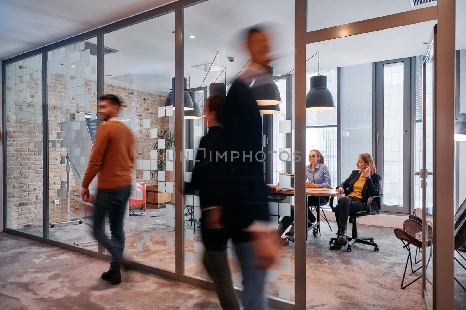 In the dynamic hustle and bustle of a business environment, a group of young business professionals walk down the corridor next to their office, while their colleagues collaborate inside, symbolizing teamwork and productivity by dotshock