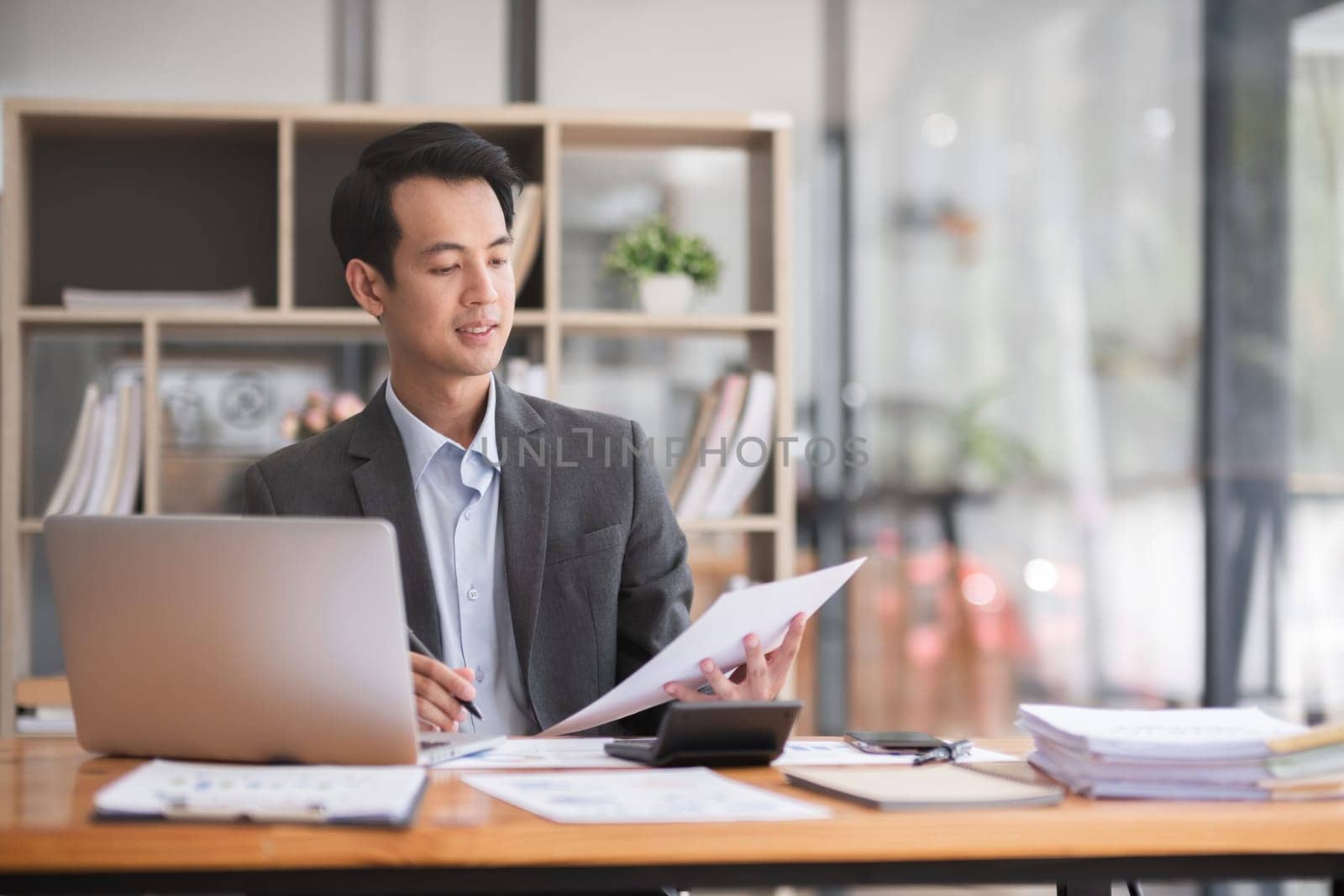 Young Asian businessman working using laptop in modern office, analyzing accounts Financial investment information report by wichayada