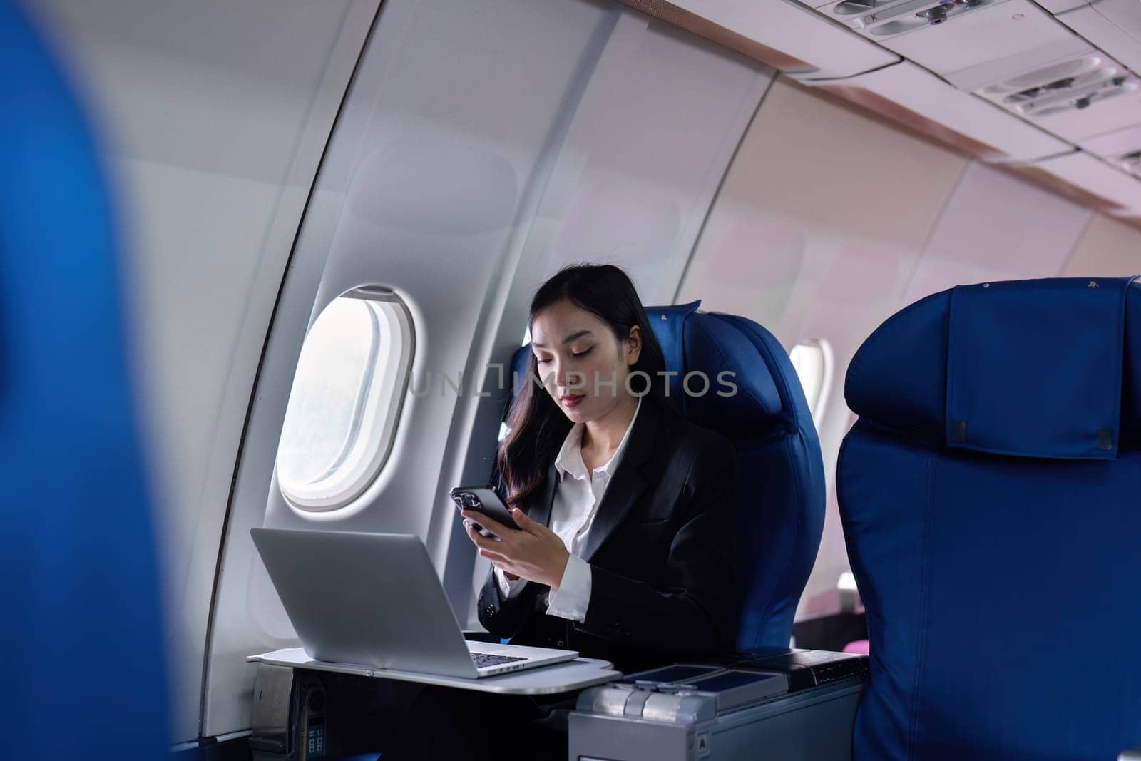 Beautiful Asian businesswoman working with laptop and mobile in aeroplane. working, travel, business concept by itchaznong