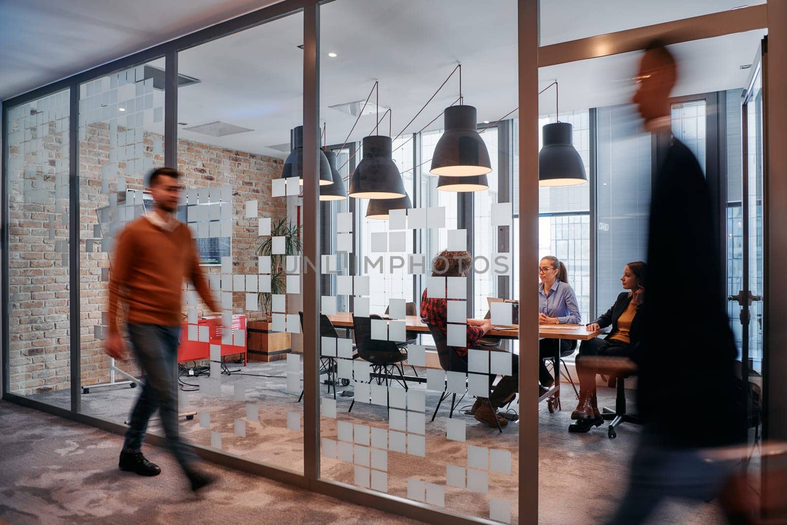 In the dynamic hustle and bustle of a business environment, a group of young business professionals walk down the corridor next to their office, while their colleagues collaborate inside, symbolizing teamwork and productivity by dotshock