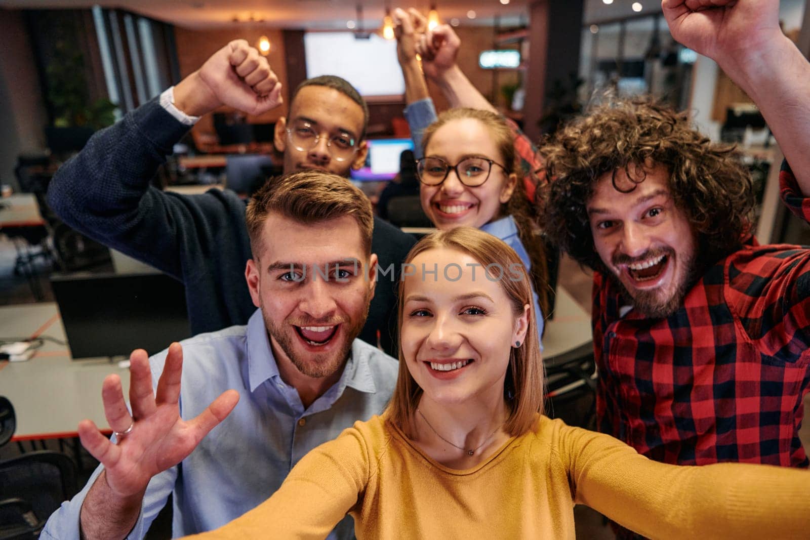 A diverse group of business professionals take a break from their tasks in a modern startup office to capture a creative selfie, showcasing teamwork and a vibrant workplace culture.
