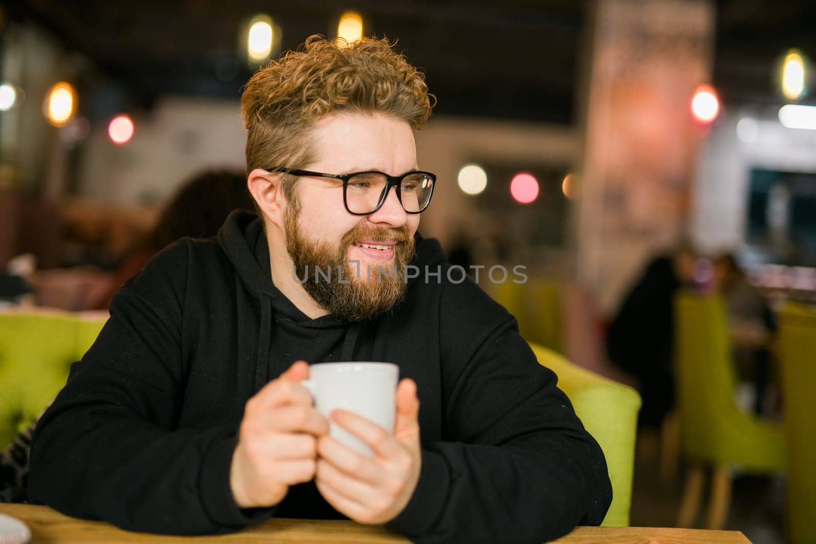 Bearded curly man smiling confident drinking coffee in restaurant or coffee shop. Millennial generation and Gen Y by Satura86