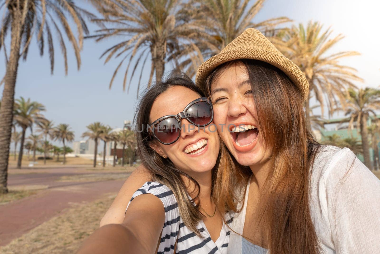 Selfie of happy two friends laughing and holding each other in the beach. Cheerful girls embracing each other. High quality photo