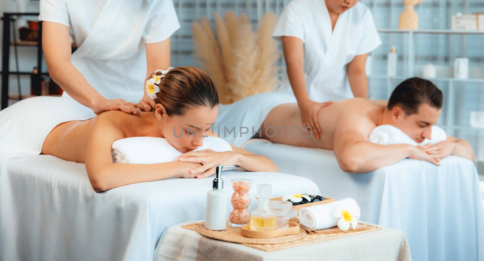Caucasian couple customer enjoying relaxing anti-stress spa massage and pampering with beauty skin recreation leisure in day light ambient salon spa at luxury resort or hotel. Quiescent