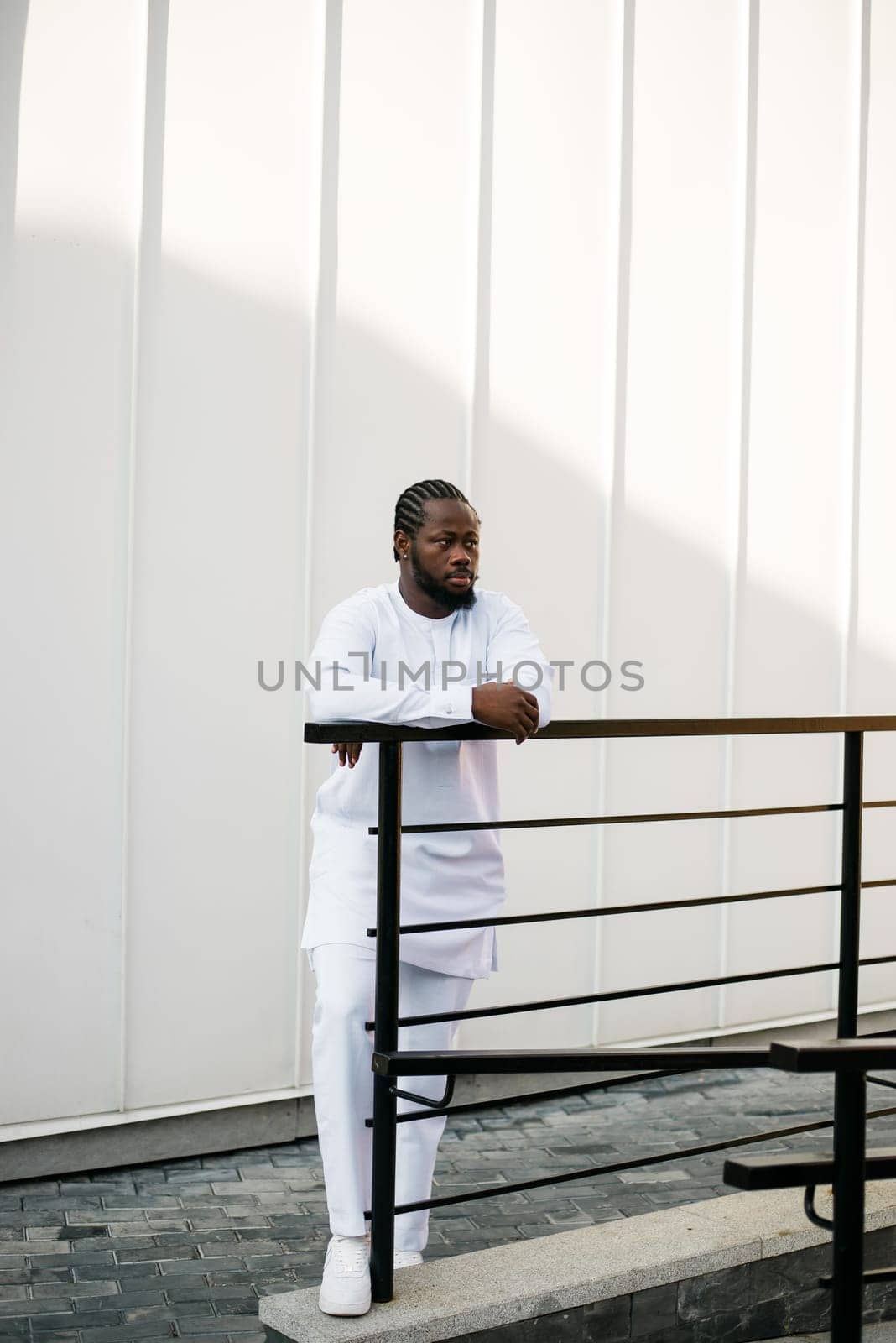 Cheerful male tourist dress in white wear dashiki ethnic smiling at city street on stairs. African American travel model have free time.
