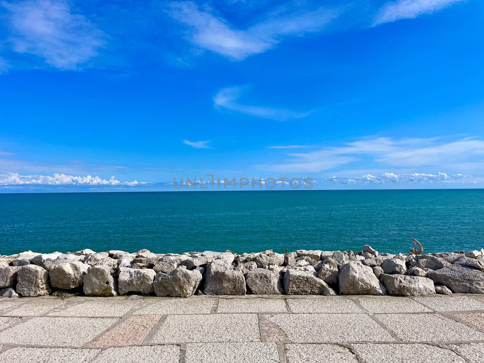 Turquoise clean calm sea under blue sky and big stones on the shore. High quality photo