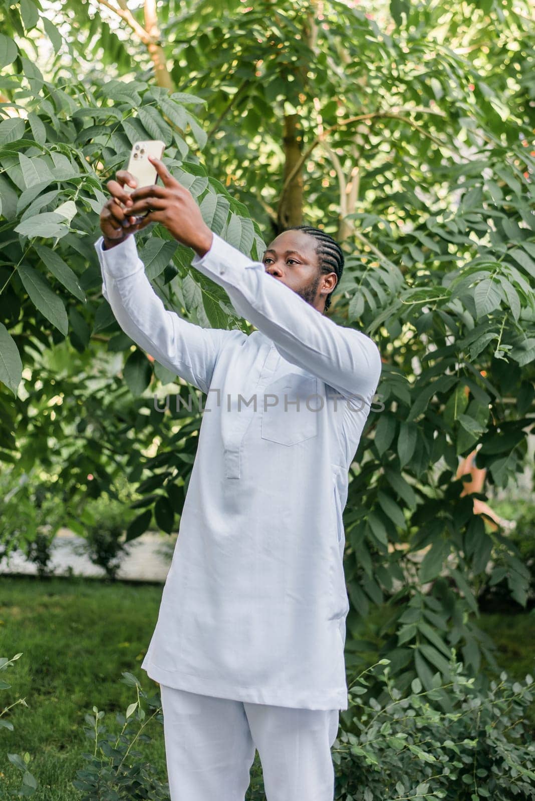 Happy young African American man in dashiki ethnic clothes taking selfie on green background outdoor in summer time. Millennial generation student and youth. by Satura86