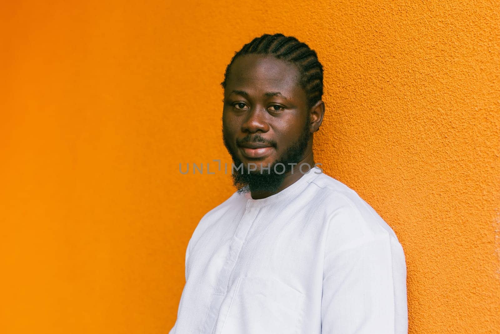 Close up portrait of a african american man smiling wearing ethnic dashiki clothes outdoor in summer street orange wall. Millennial generation student and youth. Copy space by Satura86