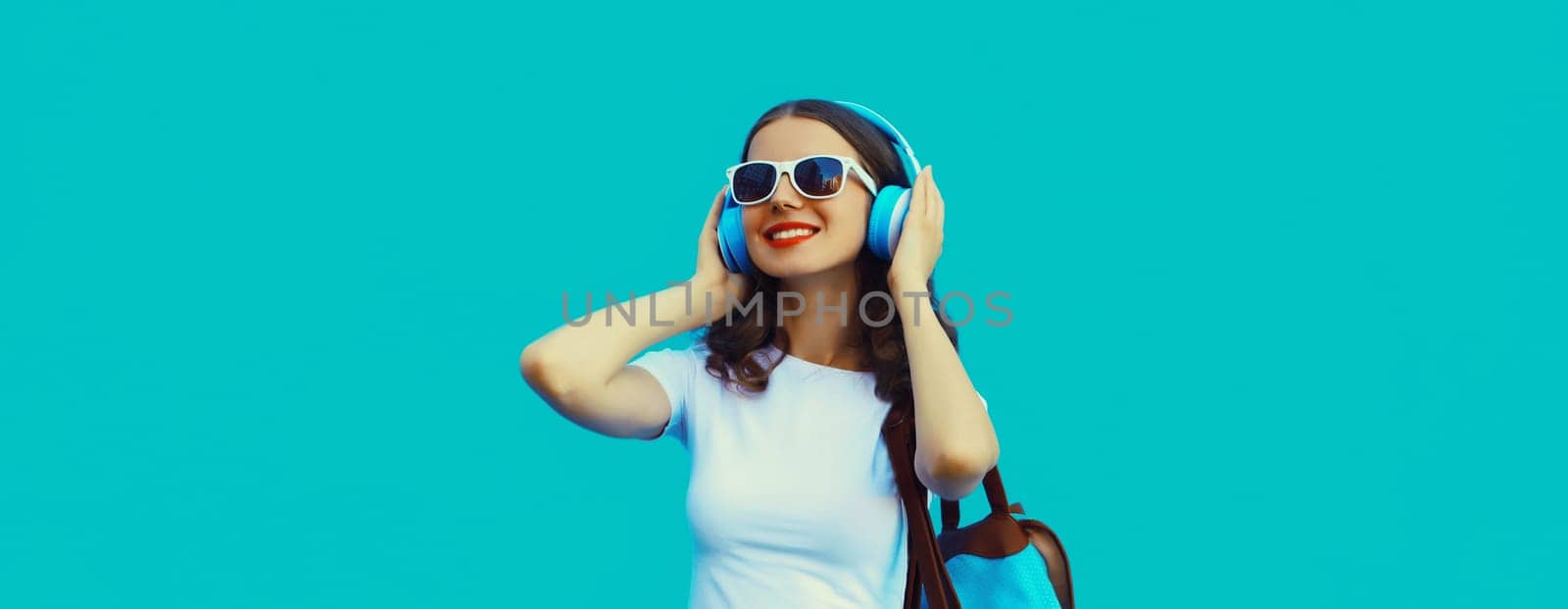 Happy modern happy young woman listening to music with headphones on blue studio background
