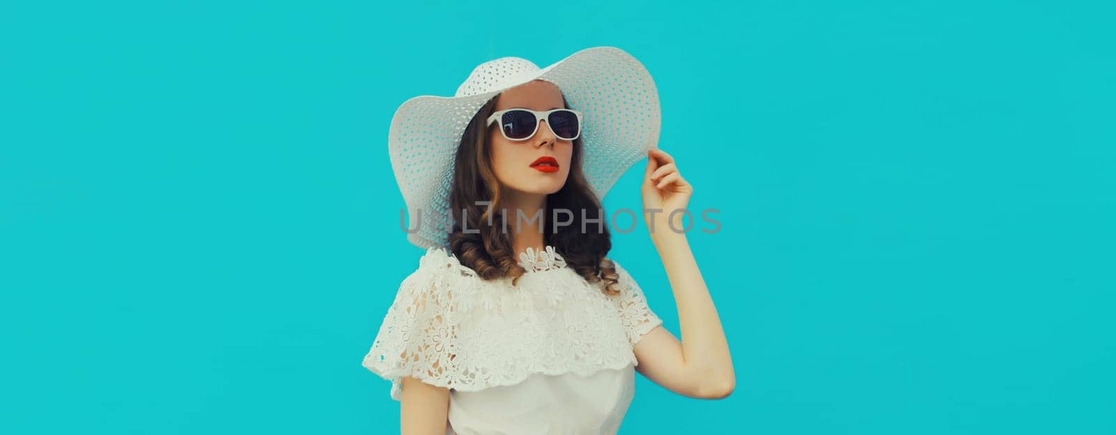 Portrait of beautiful caucasian young woman model posing wearing white summer straw hat on blue studio background