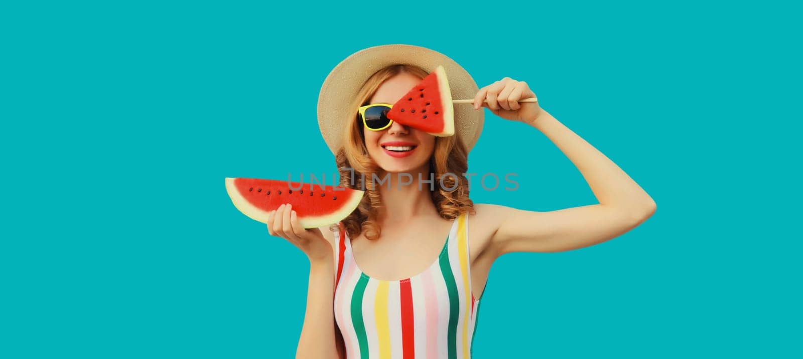 Summer portrait of happy young woman with fresh juicy fruits, lollipop and slice of watermelon wearing straw hat, sunglasses on blue background