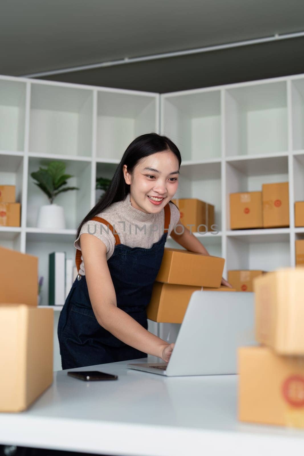 Startup small business entrepreneur of freelance Asian woman using laptop and box to receive and review order online to prepare to pack sell to customer, online business ideas by nateemee