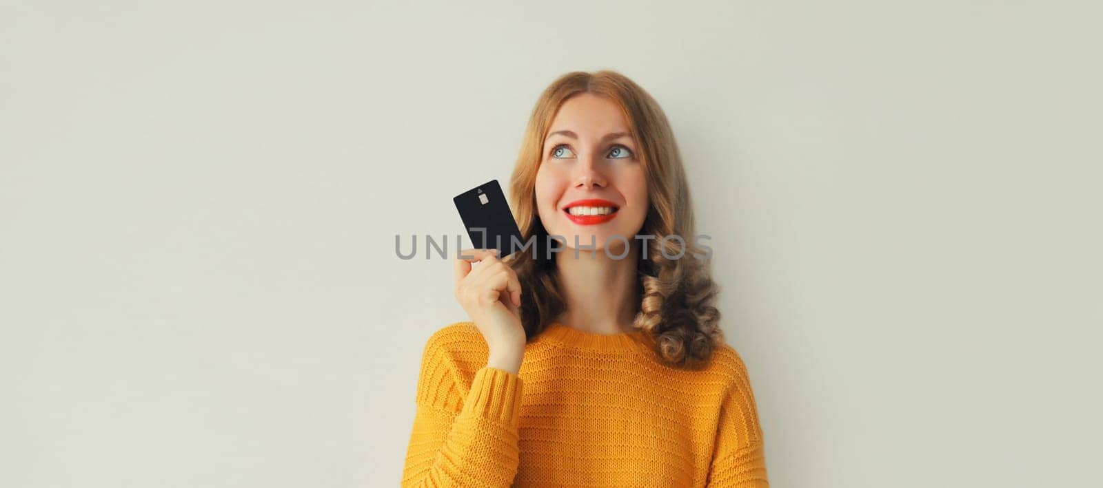 Portrait of happy smiling young woman holding plastic credit bank card and looking up on studio background