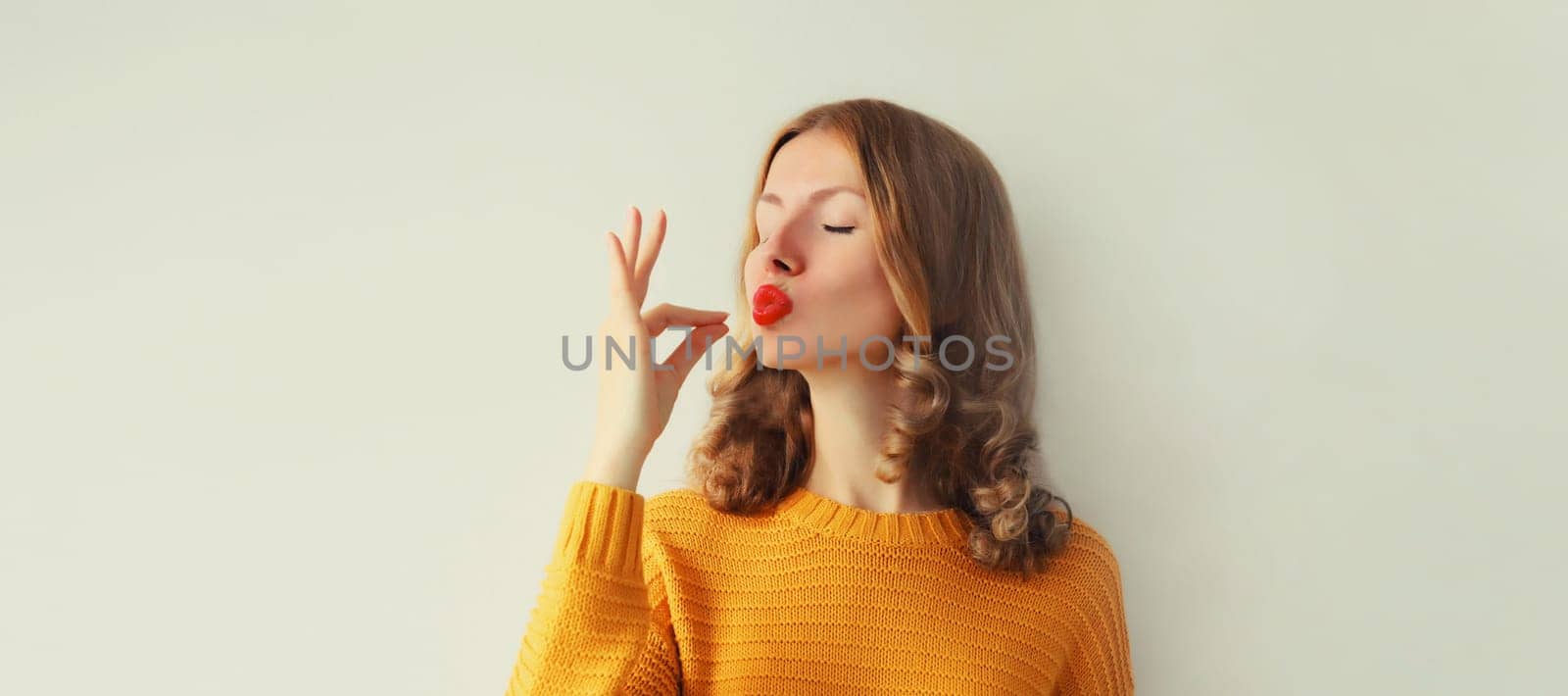 Portrait of happy young woman enjoying perfect flavor, shows gesture of delicious taste of food on studio background