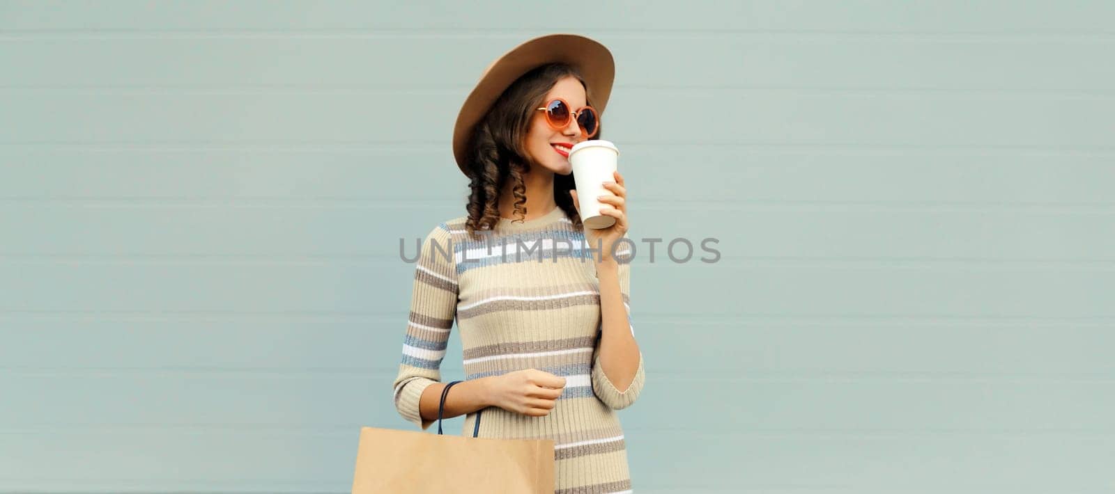 Stylish beautiful happy smiling young woman posing with shopping bags in round hat, dress on city street