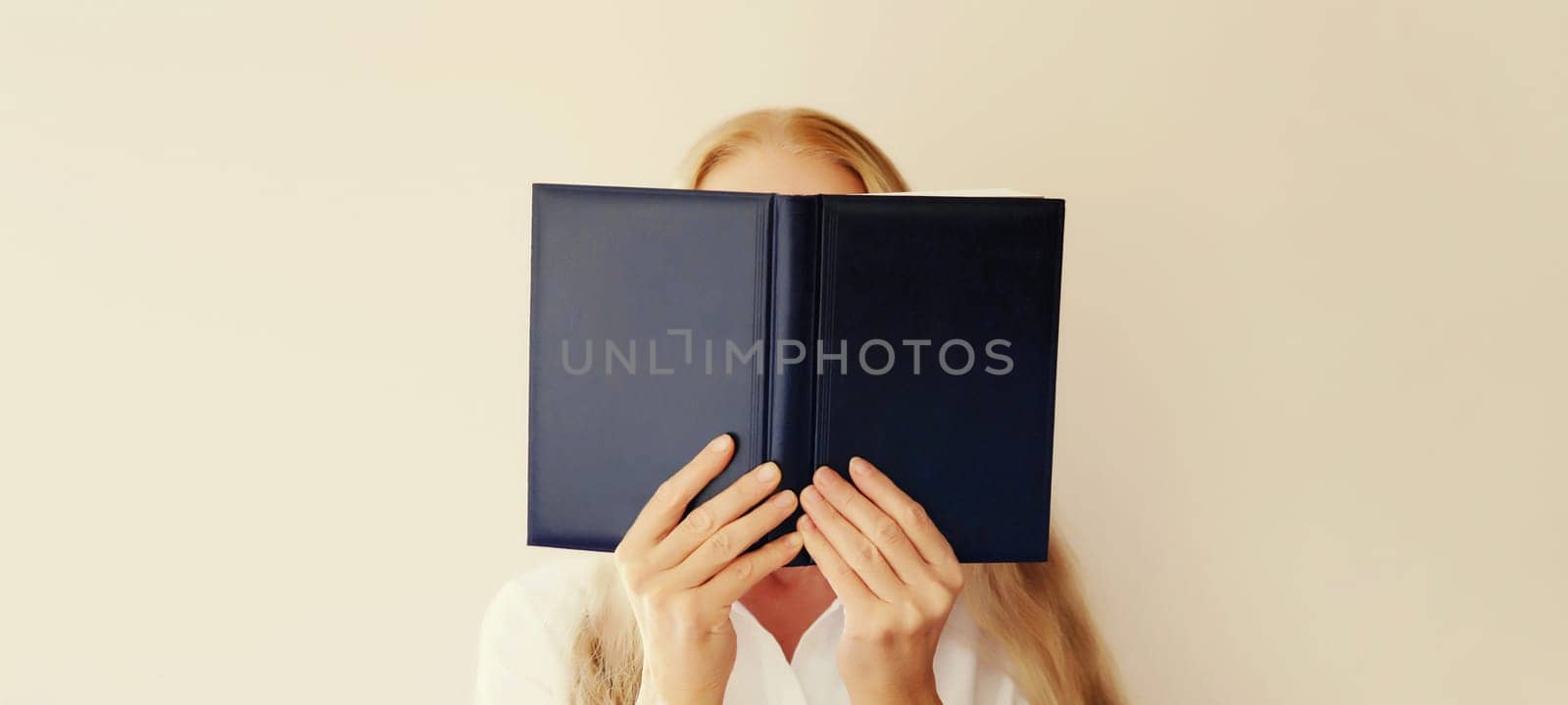 Young sad tired woman student covering her face with open book with blank cover on white background
