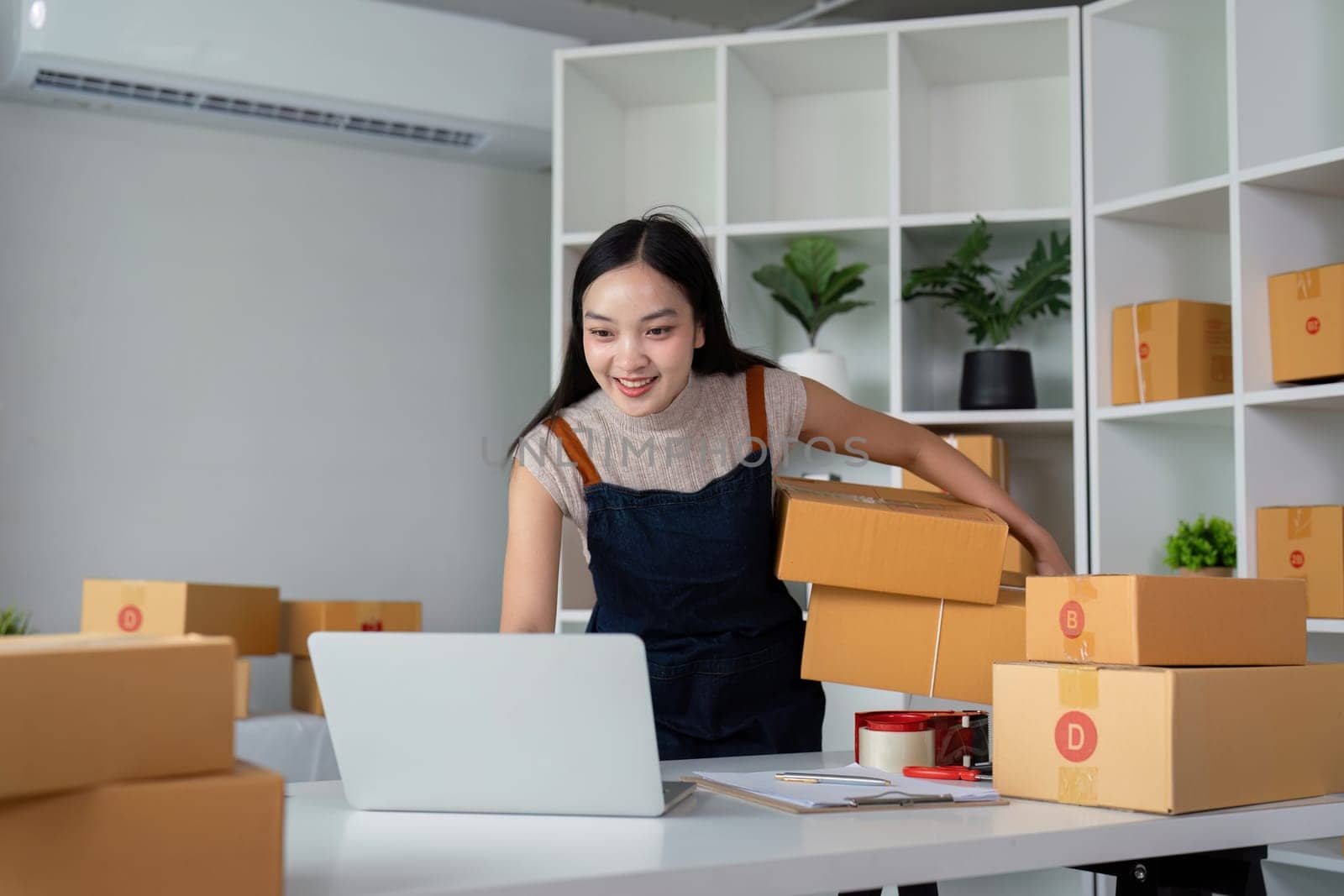 Startup small business entrepreneur of freelance Asian woman using laptop and box to receive and review order online to prepare to pack sell to customer, online business ideas.