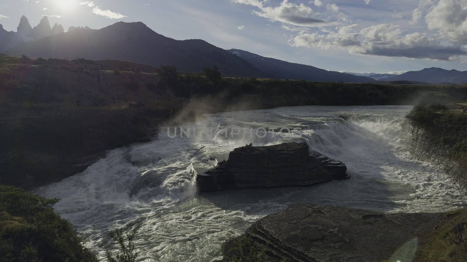 Slow-mo video captures a majestic waterfall at dusk with Torres del Paine silhouetted against the setting sun.