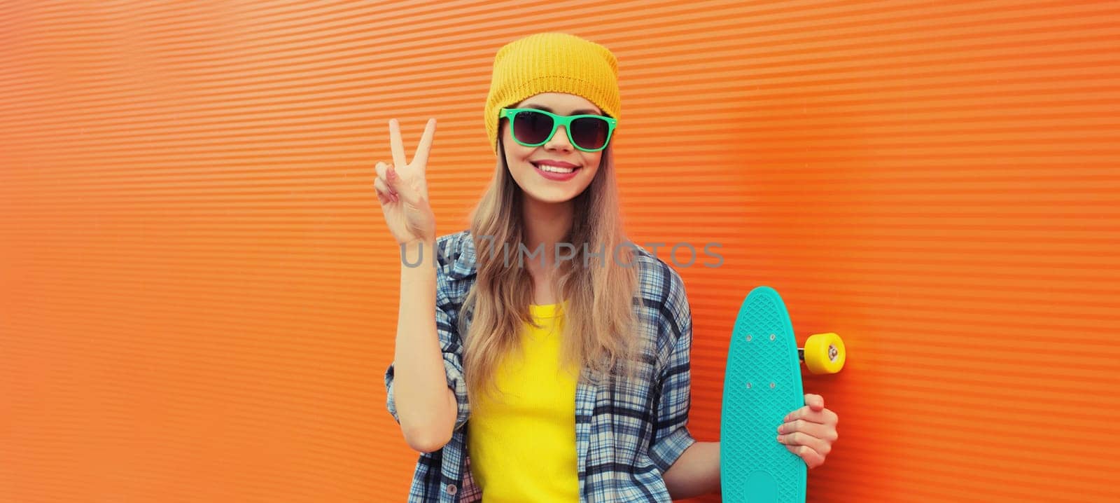 Summer portrait of happy cheerful stylish young woman with skateboard posing on orange background by Rohappy