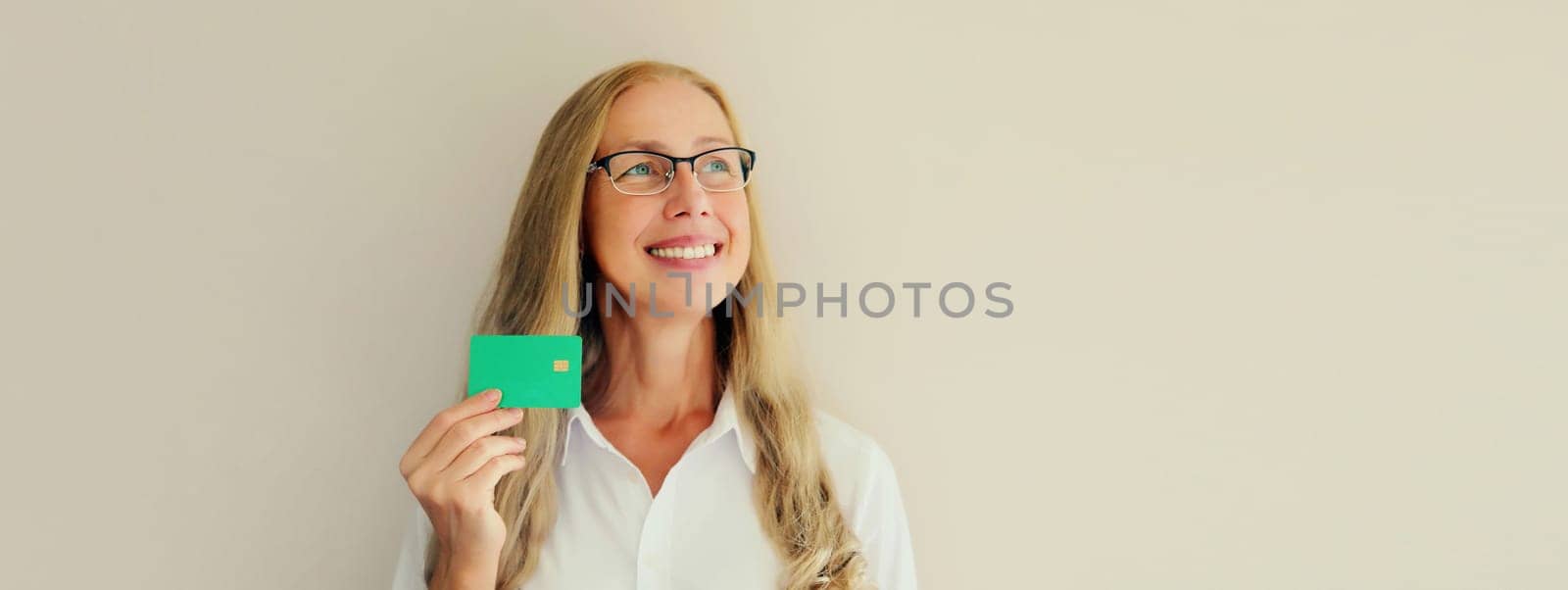 Portrait of happy successful smiling middle-aged woman holding plastic credit bank card on studio white background
