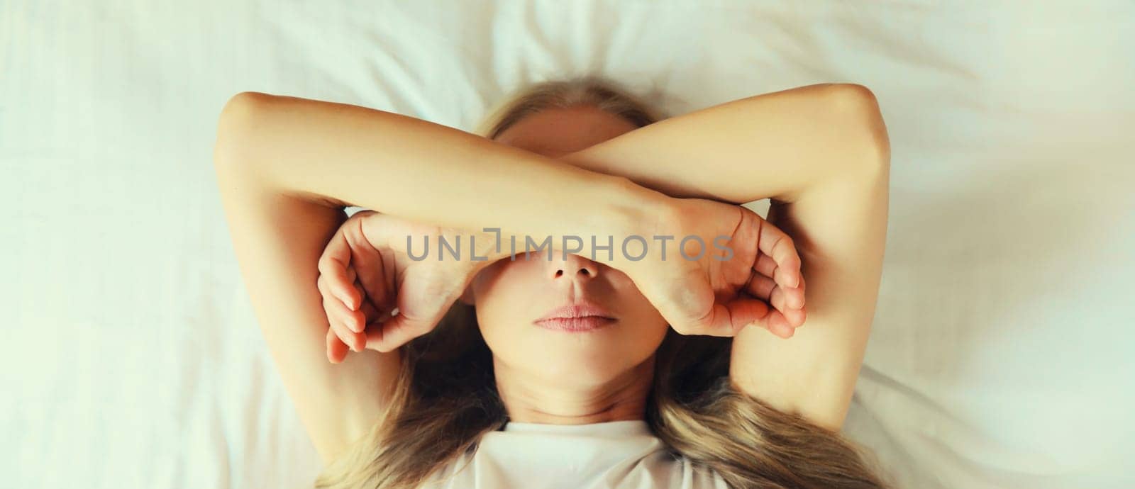 Tired sleepy woman wakes up lying on the bed on pillow in bedroom at home by Rohappy
