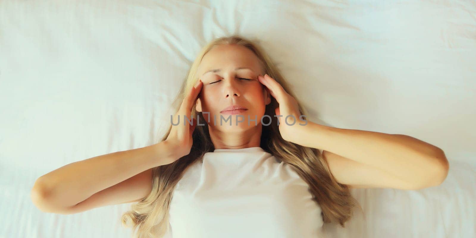 Upset exhausted woman with headache, pain tension in the head, suffers from migraine lying on the bed on pillow in bedroom at home