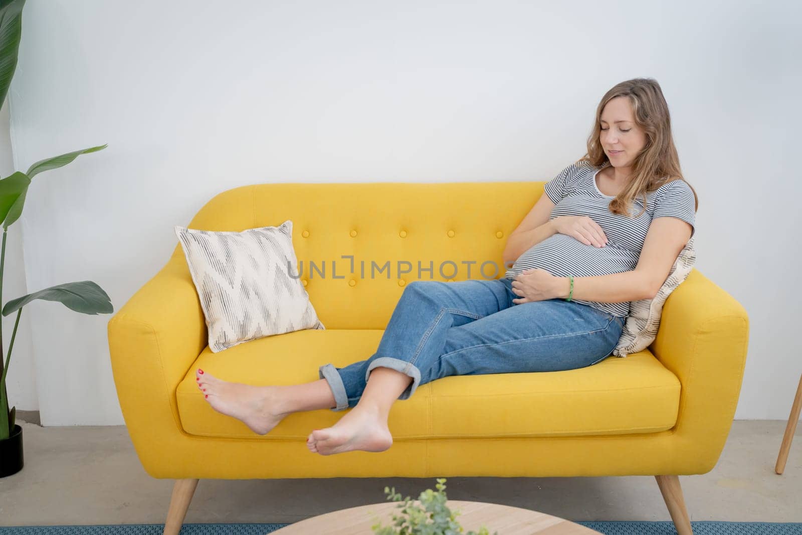 Smiling pregnant woman embracing belly in living room with copy space for text. High quality photo